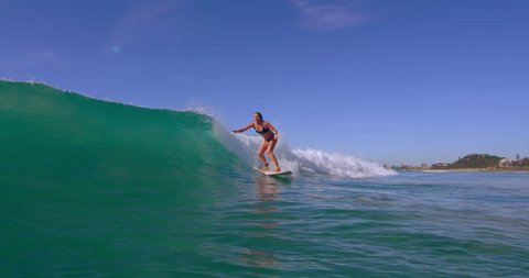 Fit blonde woman surfing a large ocean wave and having fun in Australian beach with bright day lighting. Wide shot on 4k RED camera.