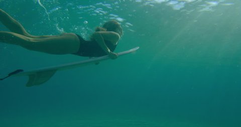 Professional female surfer diving under ocean water with surfboard in Australian beach with bright day lighting. Wide shot on 4k RED camera.
