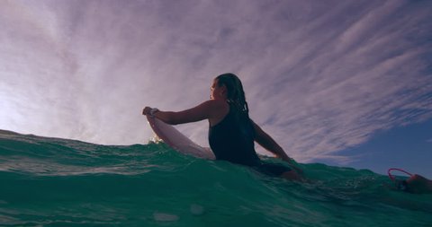 Young female surfer contemplating while lying on surfboard and swimming over an ocean wave in Australian beach with bright day lighting. Wide shot on 4k RED camera.