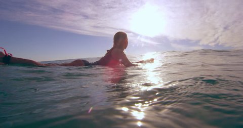 Professional female surfer swimming over an ocean wave on surfboard in Australian beach with bright day lighting. Wide shot on 4k RED camera.