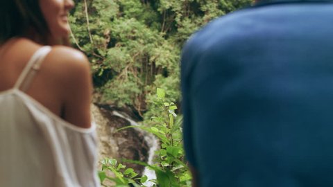 Two millennial friends chatting in front of small waterfall in an Australian rainforest path through shaded green dense treebed during daytime. Medium shot on 4k RED camera.