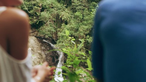 Two happy, millennial friends flirting in front of small waterfall in an Australian rain forest path through shaded green dense treebed during daytime. Medium shot on 4k RED camera.