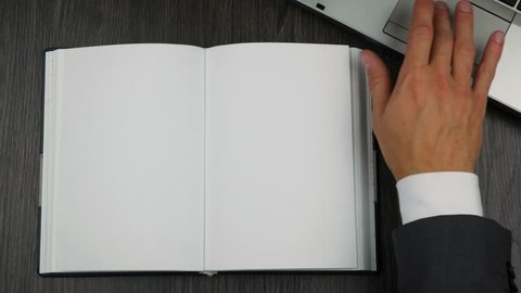 Top view of blank open diary on office table. Businessman's hand turns the page.