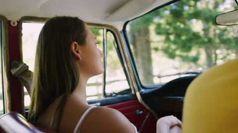 Content, young woman sits in passenger seat of vintage car as the country road passes by out window in soft focus background, in Australia in natural sunlight. Medium shot on 4K RED camera