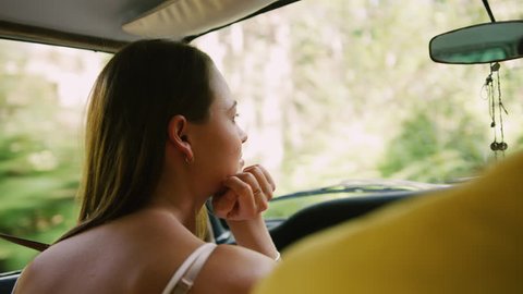 Smiling, young woman sits in passenger seat of vintage car as the country road passes by out window in soft focus background, in Australia in natural sunlight. Medium shot on 4K RED camera