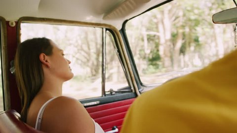 Smiling, young woman sits in passenger seat of vintage car as the country road passes by out window in soft focus background, in Australia in natural sunlight. Medium shot on 4K RED camera