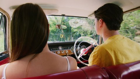 Cheery young couple drive a vintage car along a road in the country, natural daytime sunlight in Australia. Shot from the backseat, medium shot on 4K RED camera.
