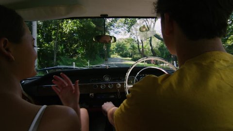 Upbeat young couple drive a vintage car along a road in the country, natural daytime sunlight in Australia. Shot from the backseat, medium shot on 4K RED camera.