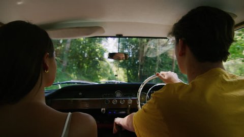 Relaxed young couple drive a vintage car along a road in the country, natural daytime sunlight in Australia. Shot from the backseat, medium shot on 4K RED camera.