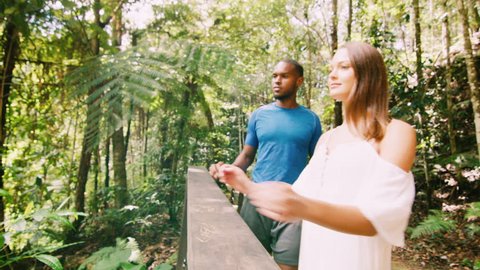 Young, happy, ethnically diverse couple walk in a forest and stop to look at the view, in Australia in natural sunlight. Medium shot on 4K RED camera.