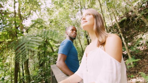 Content, young, diverse couple walk in a forest and stop to look at the view, in Australia in natural sunlight. Medium shot on 4K RED camera.