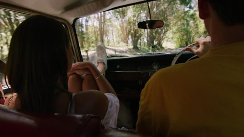 Woman hugs man as young couple drive a vintage car along a road in the country, natural daytime sunlight in Australia. Shot from the backseat, medium shot on 4K RED camera.