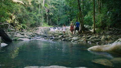 Three young ethnically diverse friends walk along the rocky bank of a stream in an Australian forest in natural sunlight. Wide shot, in 4K on a RED camera.