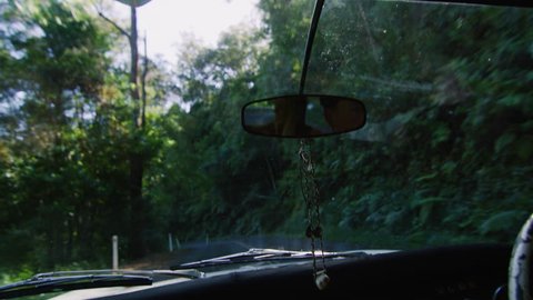 View from dashboard of vintage car, driving along country road Australian summer with happy young millennial man with hands on steering wheel. Shot in natural sunlight, medium shot on 4K RED camera.