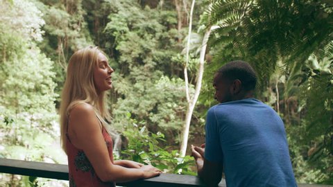 Millennial friends laughing in front of small waterfall in an Australian rainforest by safety railing during daytime. Medium shot on 4k RED camera.