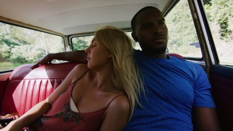 Beautiful blonde, sleeps on her handsome boyfriend's shoulder in back seat of a vintage car driving along a country road, through a forest, in Australia summer sunlight. Medium shot on 4k RED camera