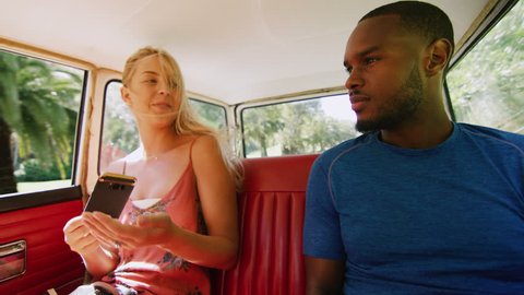 Diverse, happy couple smile, joke and talk in the back seat of a vintage car driving along a country road, through a forest, in Australian summer in natural sunlight. Medium shot on 4k RED camera