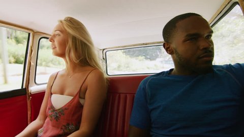 Diverse, happy couple smile, joke and talk in the back seat of a vintage car driving along a country road, through a forest, in Australian summer in natural sunlight. Medium shot on 4k RED camera