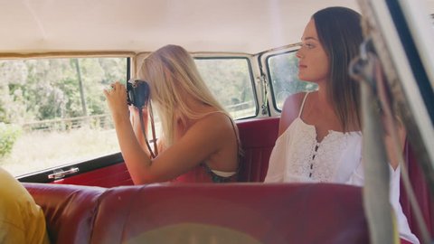 Beautiful blonde woman looks at her phone and takes selfies in backseat of a vintage car as it drives through the country in the summer, in Australia in bright daylight. Medium shot on 4K RED camera
