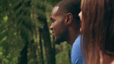 Interracial couple talking and laughing in an Australian rainforest through shaded green dense treebed during daytime. Closeup shot on 4k RED camera.