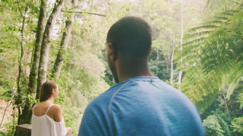 Young, happy couple look at each other lovingly and hug with spectacular view of forest, stream and waterfall in the background, in Australia in natural sunlight. Medium shot on 4K RED camera.