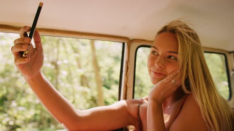 Attractive woman using mobile and takes selfies in backseat of a vintage car in the summer, in Australia in bright daylight. 