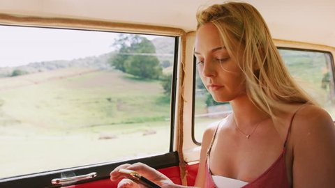 Beautiful blonde woman daydreams and looks at her phone in the backseat of a vintage car as it drives through the country in the summer, in Australia in bright daylight. Medium shot on 4K RED camera.