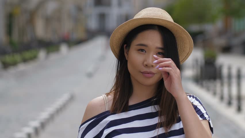 Portrait of beautiful asian girl with amazing long straight brown hair in stylish outfit smiling brightly at the camera outdoors. Cheerful elegant young asian woman posing on city street.