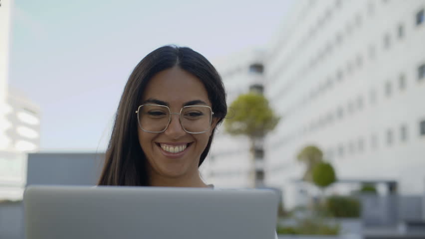 Smiling brunette businesswoman working with laptop outdoors. Latin teleworker in eyeglasses using laptop on street. Remote work concept Royalty-Free Stock Footage #1018710298
