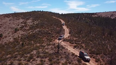 Three four wheel drive off road vehicles following a track down a hill in the Flinders Ranges in outback South Australia. Drone shot tracking over the top of the cars.