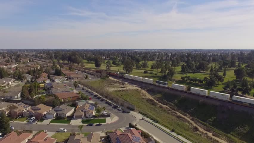 Aerial of freight train travelling alongside a residential neighborhood in Fresno, California.