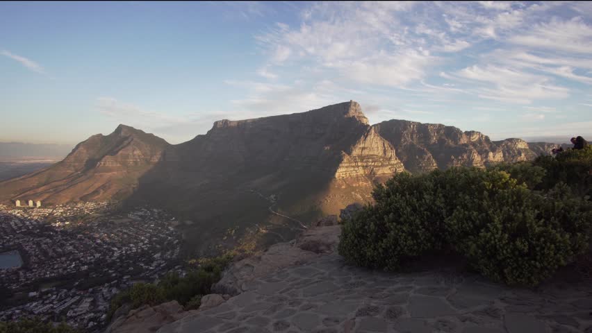 Woman walking on Top of Lions Head with Table Mountain in the background during Sunset