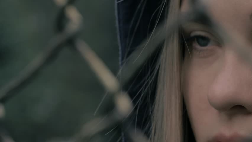 Portrait of moody and sad blonde caucasian girl behind the iron fence. Young woman behind metal fence grid jail locked
