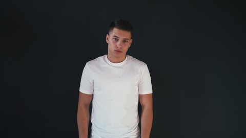 Portrait of attractive and handsome young man stands in white shirt and looks on camera. Isolated on black background. 庫存影片