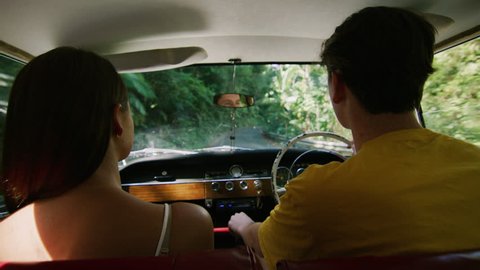 Man hugs woman as young couple drive a vintage car along a road in the country, natural daytime sunlight in Australia. Shot from the backseat, medium shot on 4K RED camera.