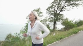 Active senior woman jogging with earbuds by the sea