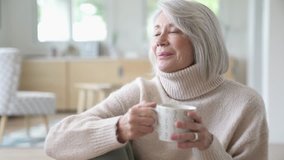 Senior woman looking relaxed at home with hot drink                              
