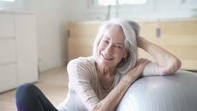 Smiling elderly woman resting on a swiss ball at home                              