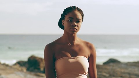 Beautiful black girl sitting by the ocean on beach in Australia during a warm day. Medium Shot on 4k RED Camera