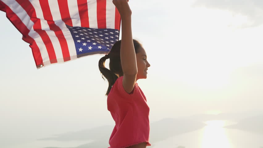 Child girl is running with USA American flag at sunset