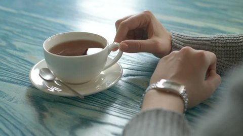 Elegant watch on a female hand against the background of a cup of tea