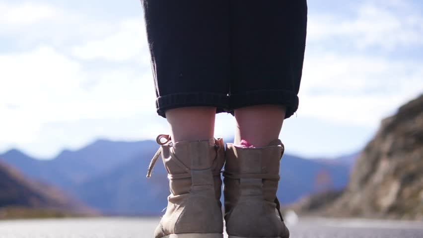 A woman with a hat walking along a mountain road. Legs gradually move away from the camera. Legs closeup