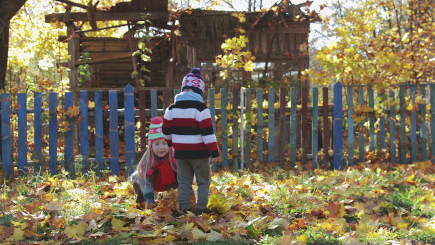 Rural, cheerful children, brother and sister play and throw up yellow, autumn leaves. They have matching hats and scarves. Family walks in the fresh air in the forest