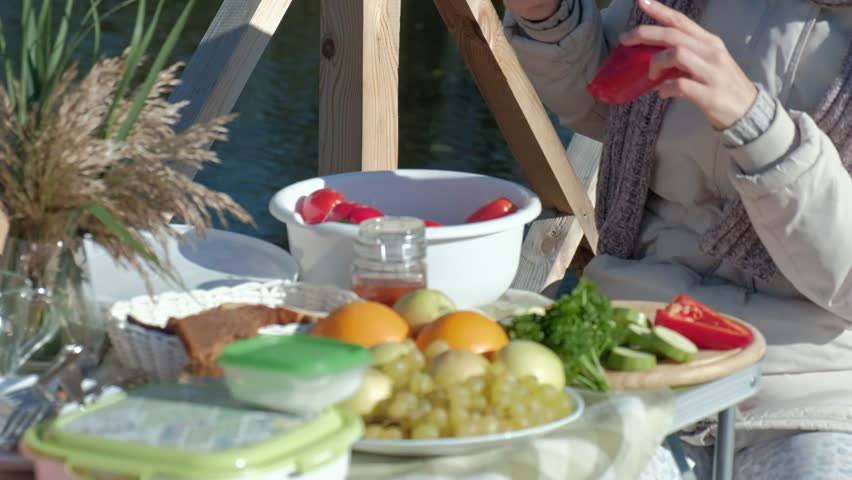 young woman in warm clothes, a picnic by the river on a wooden bridge, cutting vegetables, weekends, cold weather, outdoor recreation, tourism,close up 4k