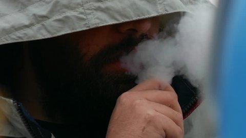 Close up of a bearded young man smoking with a hat covering his face