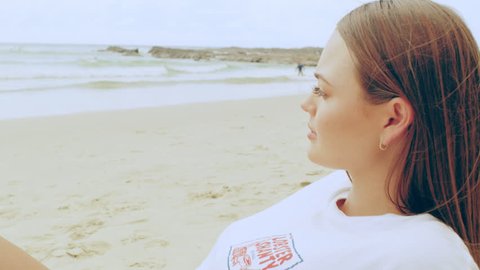 Beautiful young strawberry blonde woman wearing cut off jean shorts and t-shirt lays on a towel on the beach on Australian summer day. Medium shot in 4K on a RED camera.