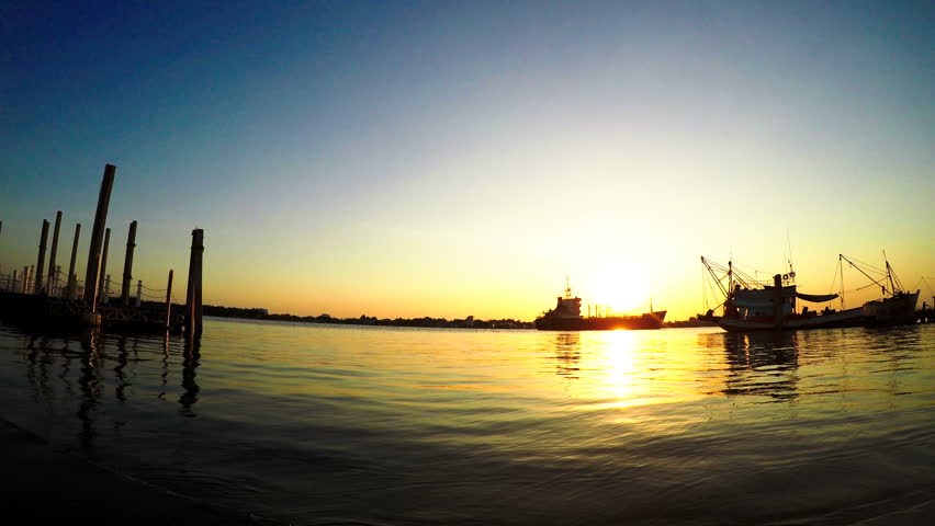 Time lapse sunset at port with a large ship and fishing boat, Twilight sky color and golden sunlight reflected on sea water.