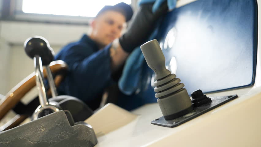 Young handsome professional guy (male) cleaner, washes the yacht after polishing and lining ceramics on the yacht. Concept of: Ceramics, Cleaning, New Ship, Polishing, Cleaner, In Robe, Cap, Hard Work
