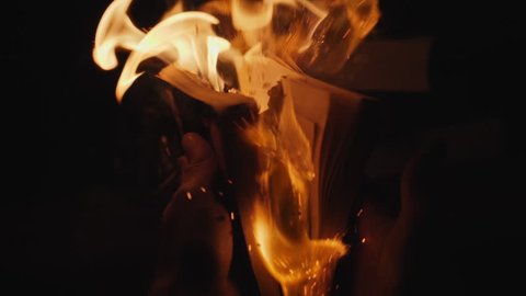 Male hands open a burning book in the dark in slow motion. Reverse video