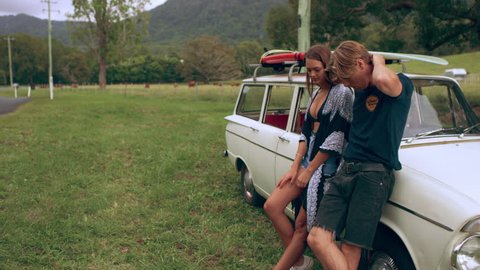 Young black woman takes a red gas can from the back of a vintage white car and walks down the road as her friends wait at the car on an overcast summer day in Australia. Medium shot on 4k RED camera